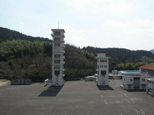 細長い建物（11階建てと、5階建てくらいの白い建物）がアスファルトの広場に立っている。